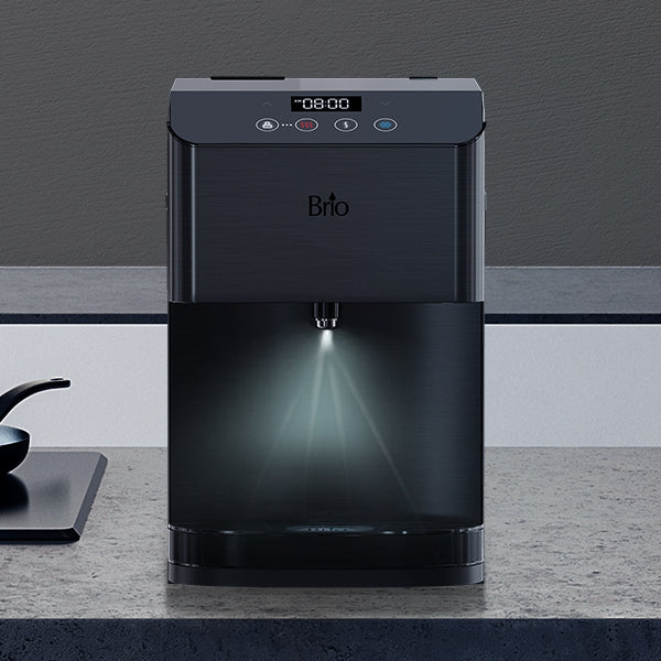 A black Brio water dispenser sits on a gray countertop, dispensing water with a light illuminating the water stream; touch buttons and a digital display are visible on the front panel.